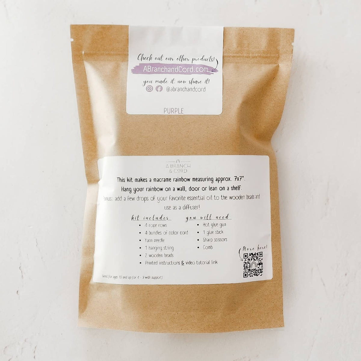 A Branch & Cords Very Berry DIY Rainbow Beginner Macrame Kit comes in a brown paper bag labeled with kit contents, required supplies, and instructions featuring a QR code for an easy macrame rainbow crafting experience.