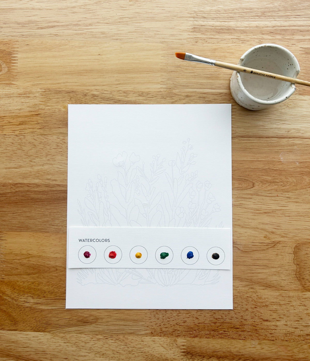 The Butterflies All-In-One Beginner Watercolor Kit by Breathe People includes floral-outlined paper, a WATERCOLORS strip with six paint dots, a brush, and water cup—everything beginners need to create art.