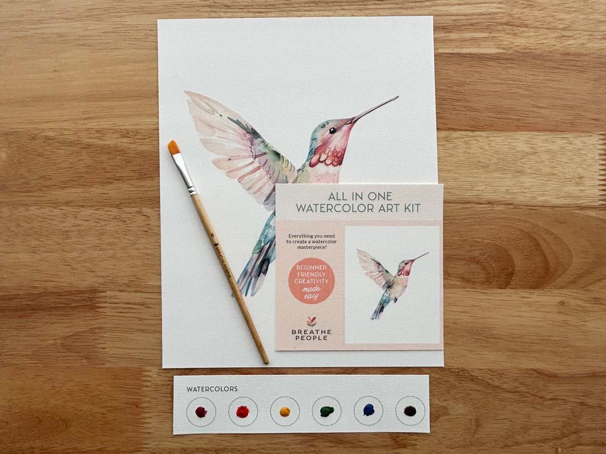 The Breathe People All-In-One Beginner Watercolor Kit - Hummingbird features a painted hummingbird, paintbrush, card, and six watercolor paint dots—perfect for beginners seeking an easy and creative art experience.