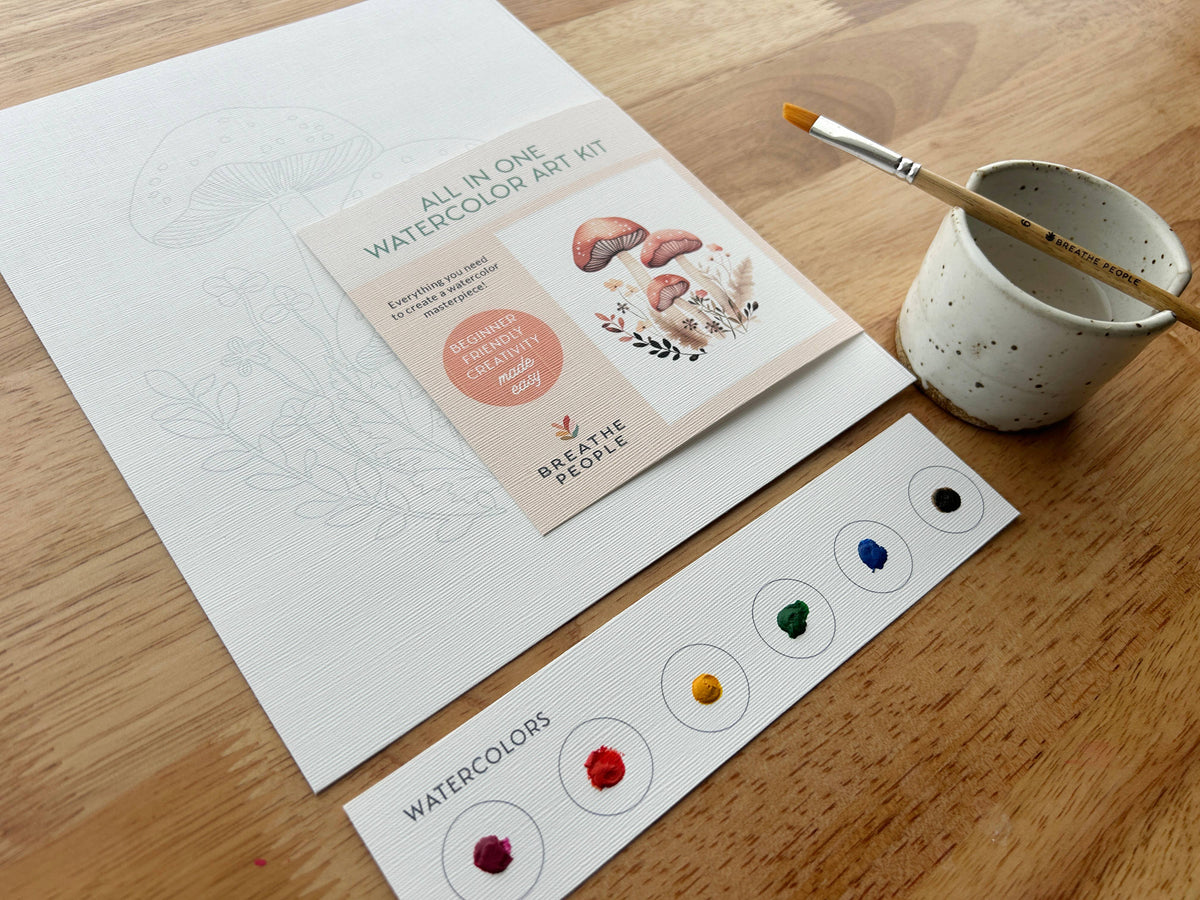 The Mushroom Forest All-In-One Watercolor Kit by Breathe People includes a paintbrush in a ceramic cup, six-color palette, mushroom illustration outline on paper, and an instruction card with mushroom artwork.