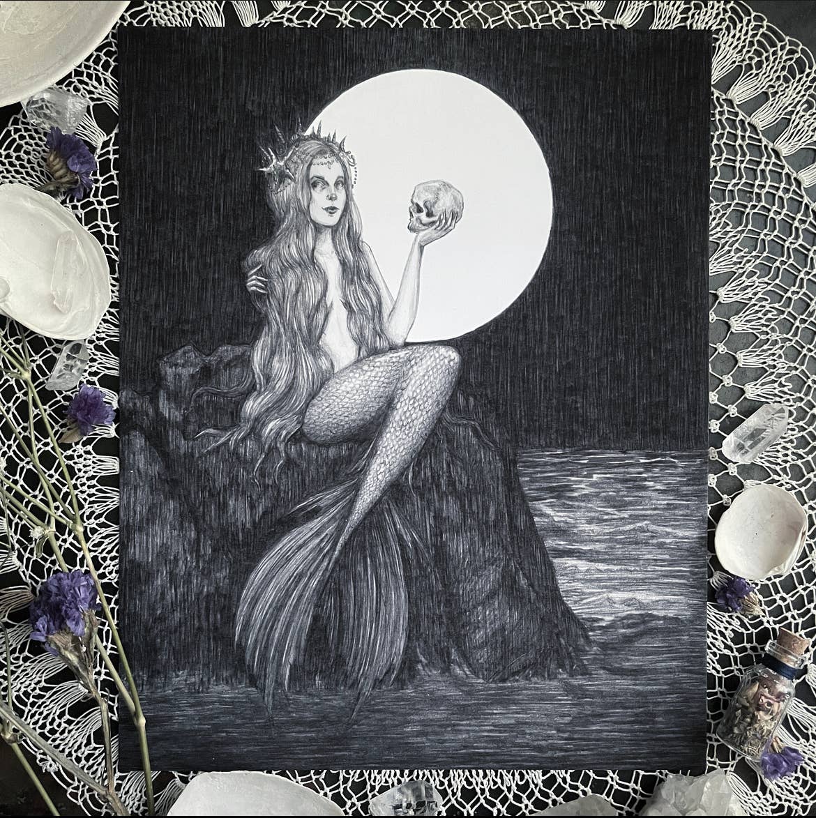 “Ondine” Fine Art Print by Caitlin McCarthy Art (10 x 8) features a Gothic Mermaid with long hair on a rock, holding a skull under the full moon, surrounded by seashells, flowers, and lace—ideal for unique fine art decor.