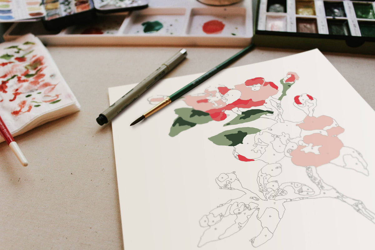 The Cate Paper Co. DIY Art Cherry Blossoms Paint-By-Numbers Kit features a partially painted floral design on a table, surrounded by a pen, paintbrush, and acrylic paints. Red blossoms and green leaves are in progress on the artwork.