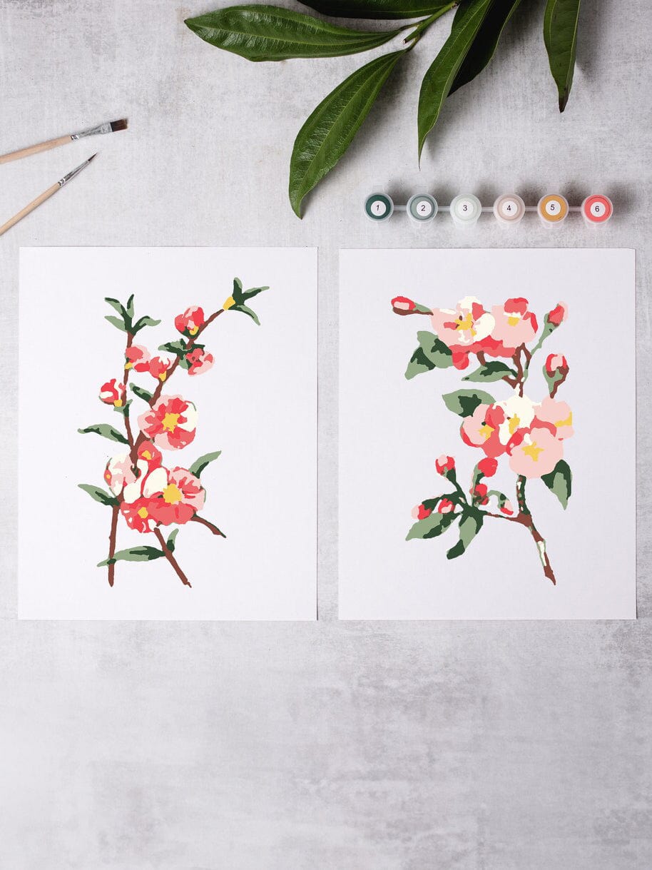The DIY Art Cherry Blossoms Paint-By-Numbers Kit by Cate Paper Co. features two floral paintings with pink and yellow blossoms, displayed alongside paintbrushes and acrylic paints on a light gray surface.