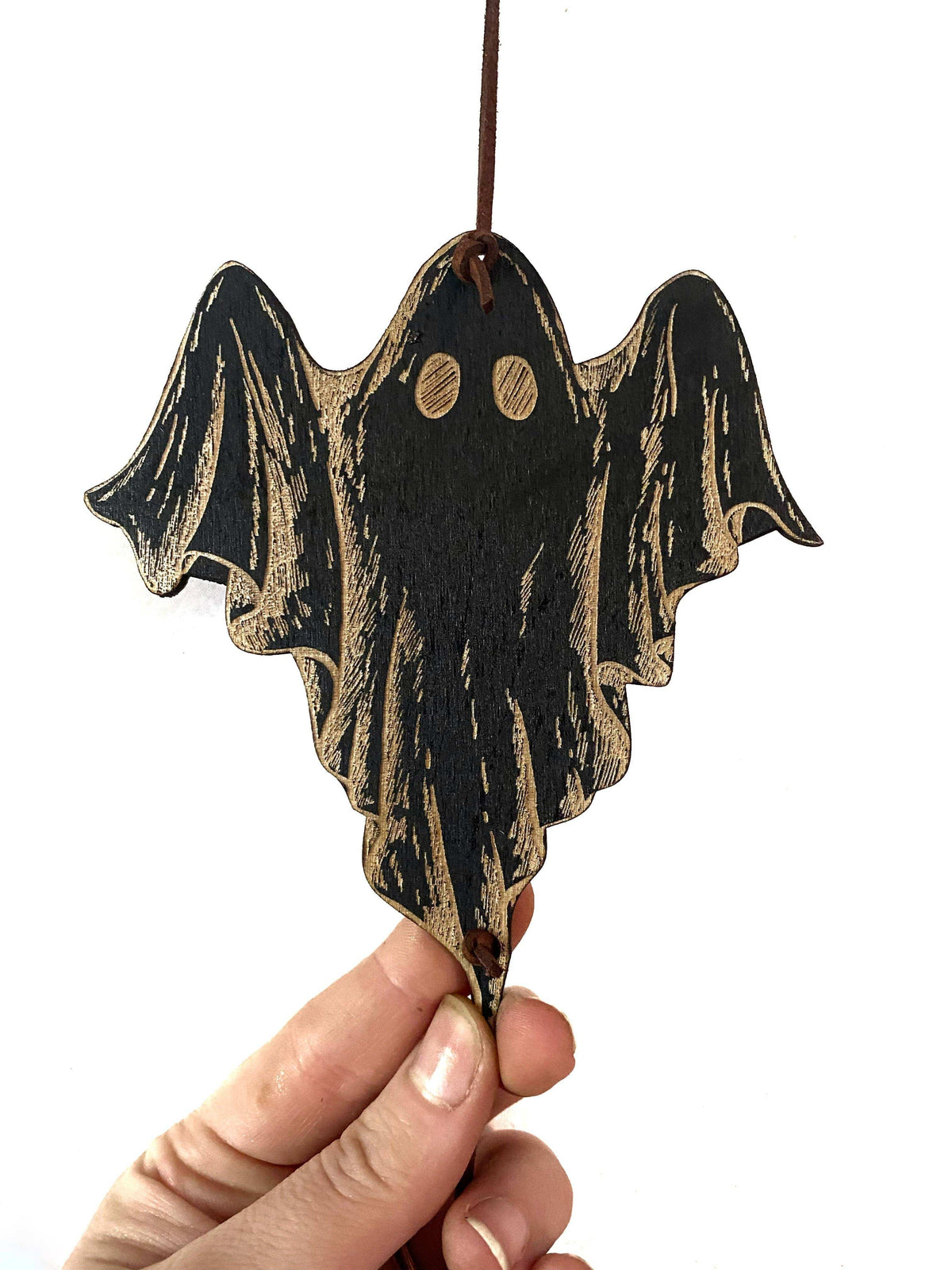 A hand holds the CSAcreative Ghost Garland, a dark wood ornament with engraved details and two round eyes—ideal for Halloween decor or as unique ghost wall art, shown against a white background.
