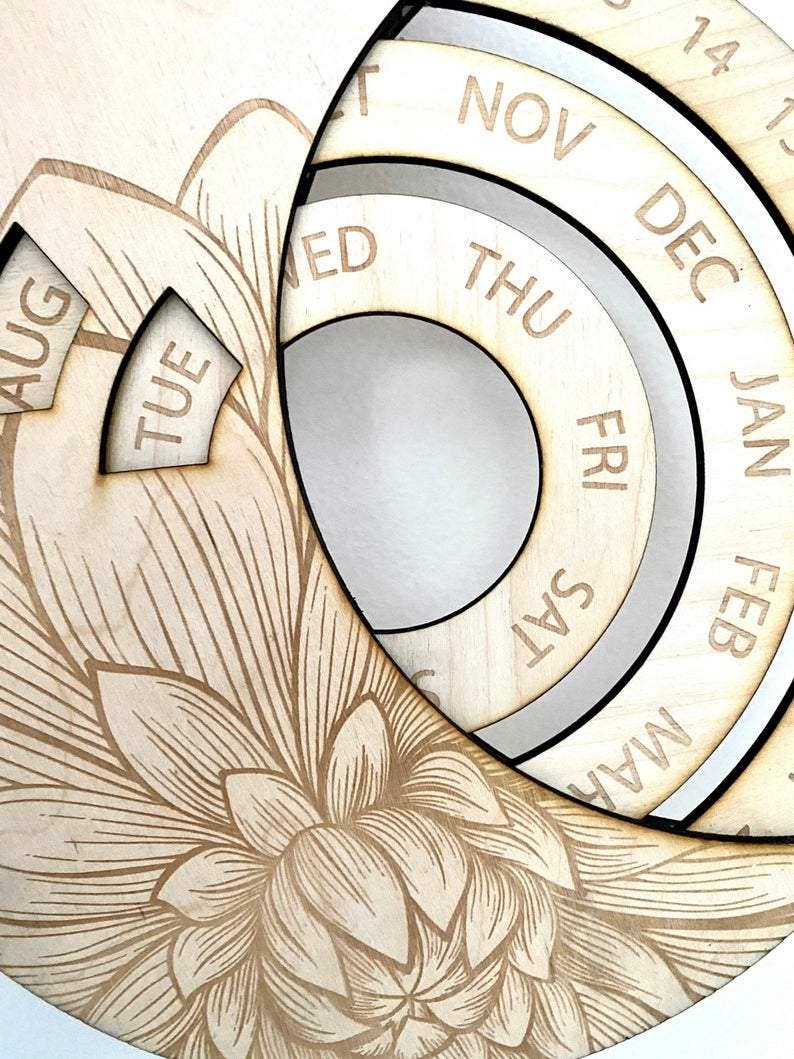 A close-up of the CSAcreative Perpetual Calendar, a unique wooden piece with engraved months, days, and dates in circular sections, plus a detailed floral design etched in the bottom left corner.