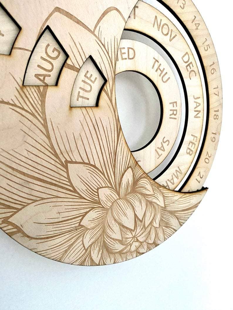 The CSAcreative Perpetual Calendar is a circular wooden piece with laser-engraved floral patterns, featuring part of a lotus flower and labeled day and month sections for sustainable, handcrafted beauty.