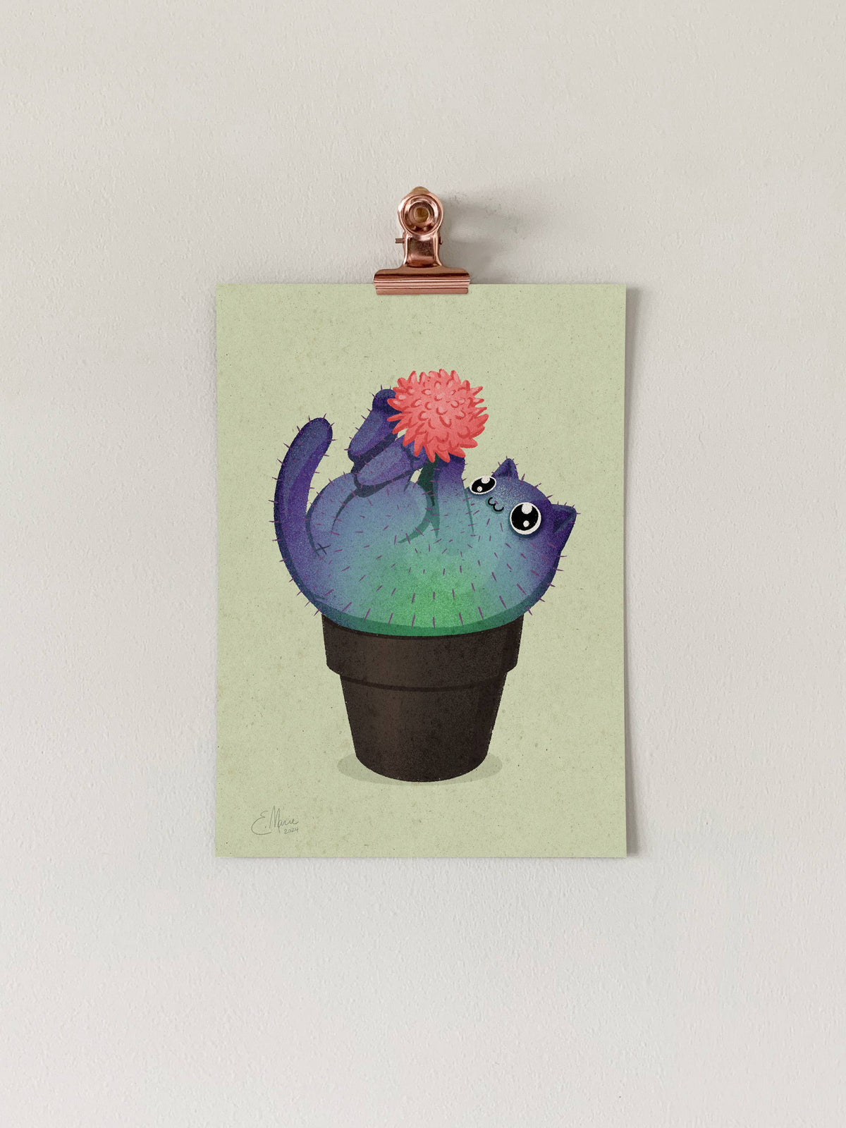 The Coral Prickly Purr Catcus Art Print (7 x 5) by Elissa Marie Creative features a playful, round green cat-shaped cactus with a pink flower in a black pot, clipped to a light wall for a charming display.