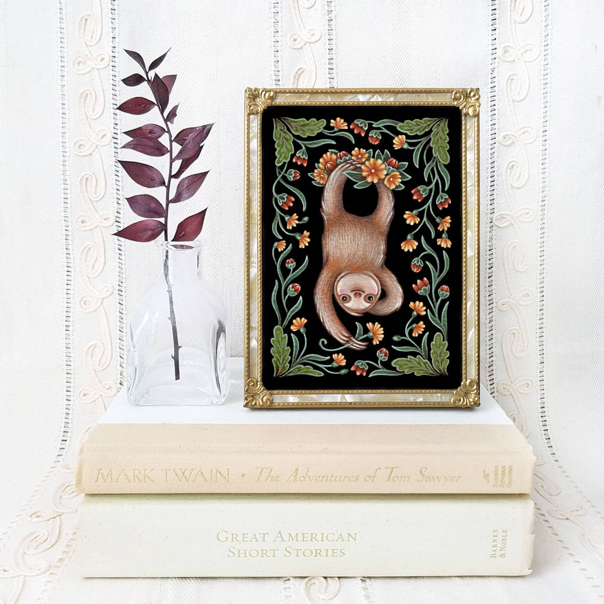 The *Retiring* Sloth Folk Art Print by Faina Lorah features a watercolor sloth on stacked books with a glass vase and dried leaves, set against lace. Available in multiple sizes.