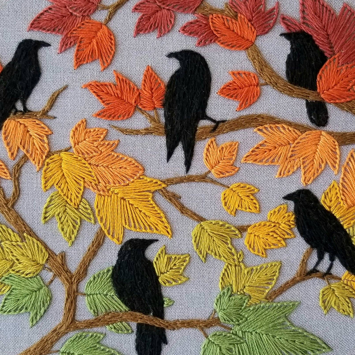 The 6 Beginner Autumn Birds Embroidery Kit by Jessica Long Embroidery features five black crows on branches with colorful fall leaves against a light gray fabric, ideal for beginners or as a unique fall leaves craft.