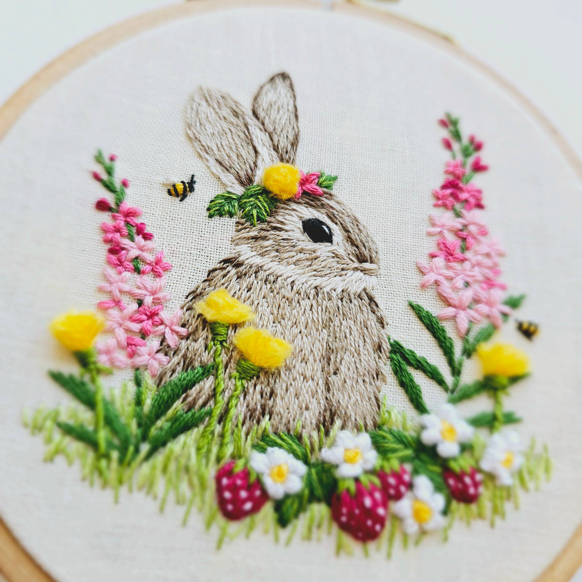 The *Late May Pre-Order* 4 Berry Patch Bunny Embroidery Craft Kit by Jessica Long Embroidery features a hand-embroidered bunny in a flower crown among colorful blooms, strawberries, and bees, all displayed in a wooden hoop.
