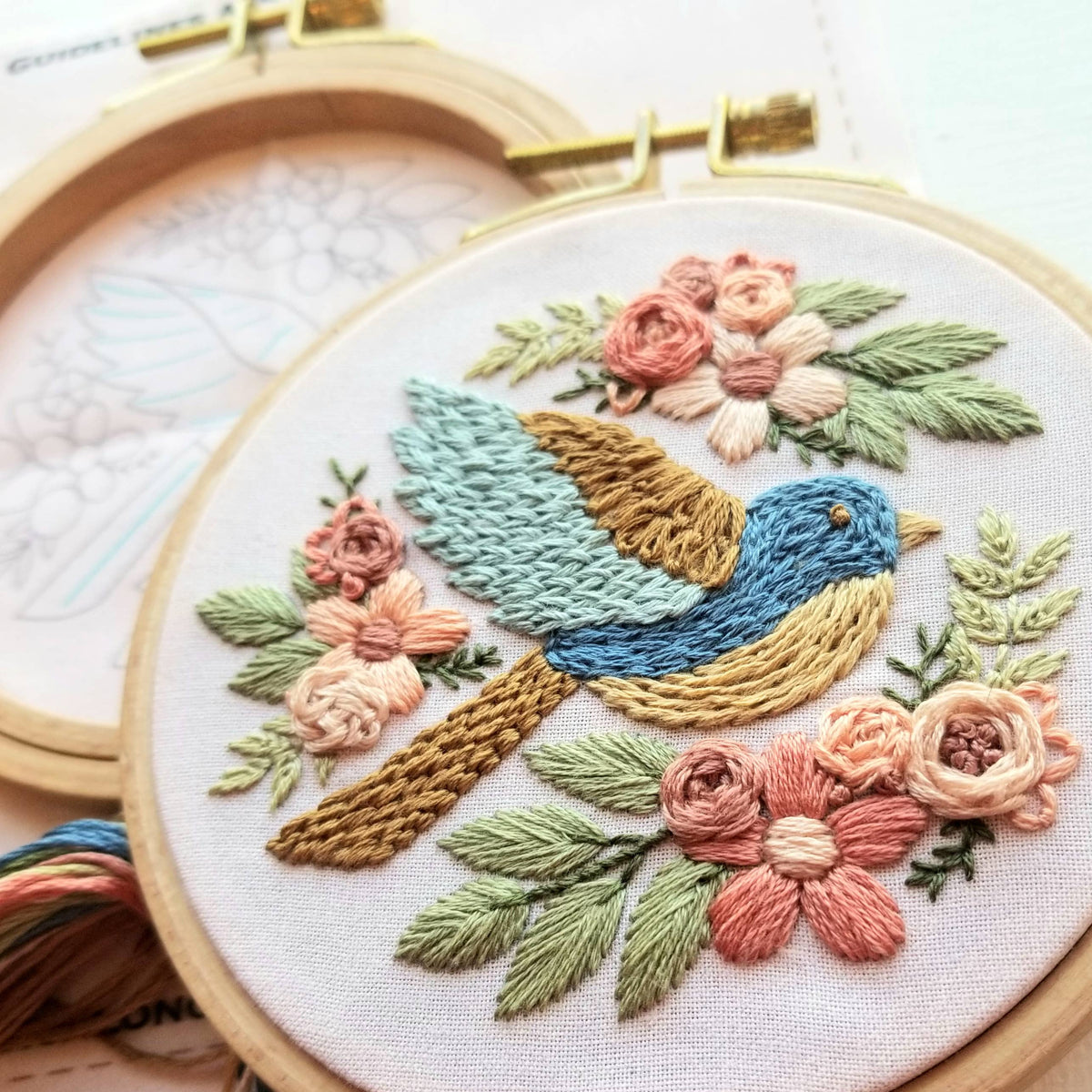 The 4 Beginner Bluebird Sampler Embroidery Kit by Jessica Long Embroidery features a colorful bluebird with pink, peach, and cream flowers on white fabric—includes visible pattern and thread, perfect for beginners to create their own sampler.