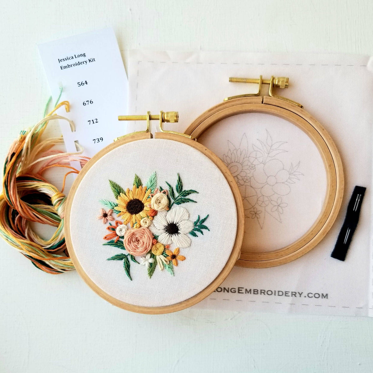 The 4 Beginner Cozy Harvest Embroidery Kit by Jessica Long Embroidery includes a finished floral hoop, empty hoop, embroidery floss, needle, and printed flower fabric—everything you need to start stitching.