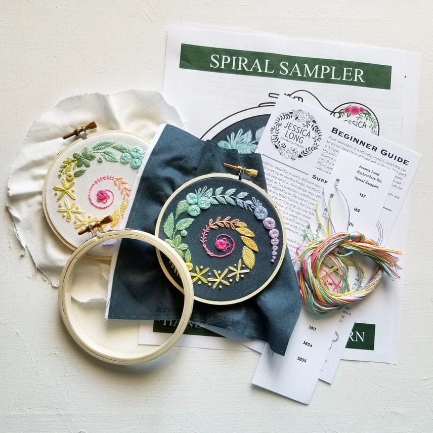 The Jessica Long Embroidery 4 Beginner Ivory Spiral Sampler Kit includes two spiral hoop art pieces, a wooden hoop, pastel floss, beginner instructions, and printed guides—perfect for a relaxing hobby.