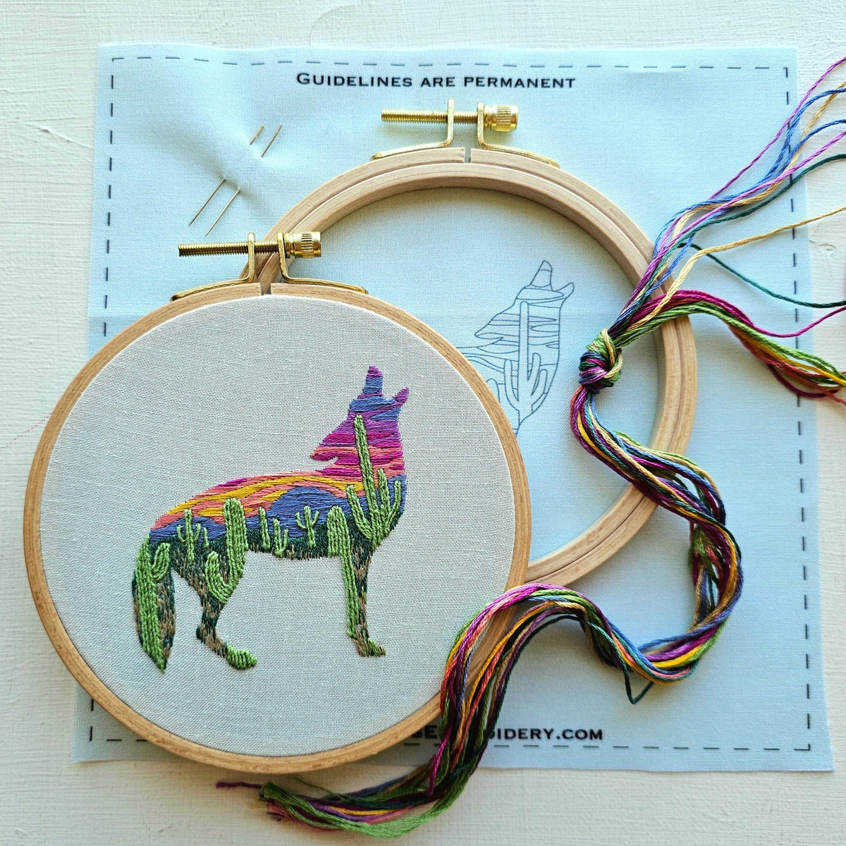 The 5 Beginner Desert Coyote Embroidery Kit by Jessica Long Embroidery features a round hoop with a vibrant coyote and cactus design. Perfect for beginners, it includes needle, thread, empty hoop, and a printed fabric guide.
