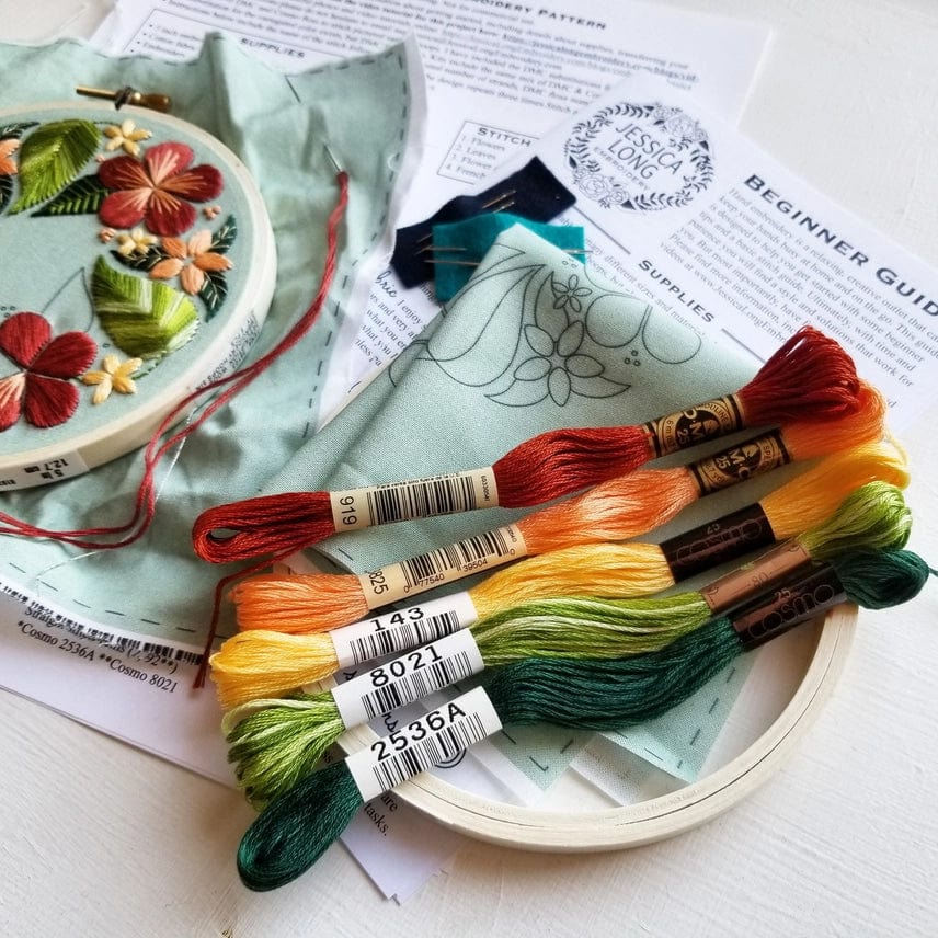 The Jessica Long Embroidery *Late May Pre-order* 5 Beginner Green Floral Flourish Embroidery Kit includes a floral fabric in a hoop, colorful threads, an extra fabric piece, and beginner instructions—perfect for hoop art projects.