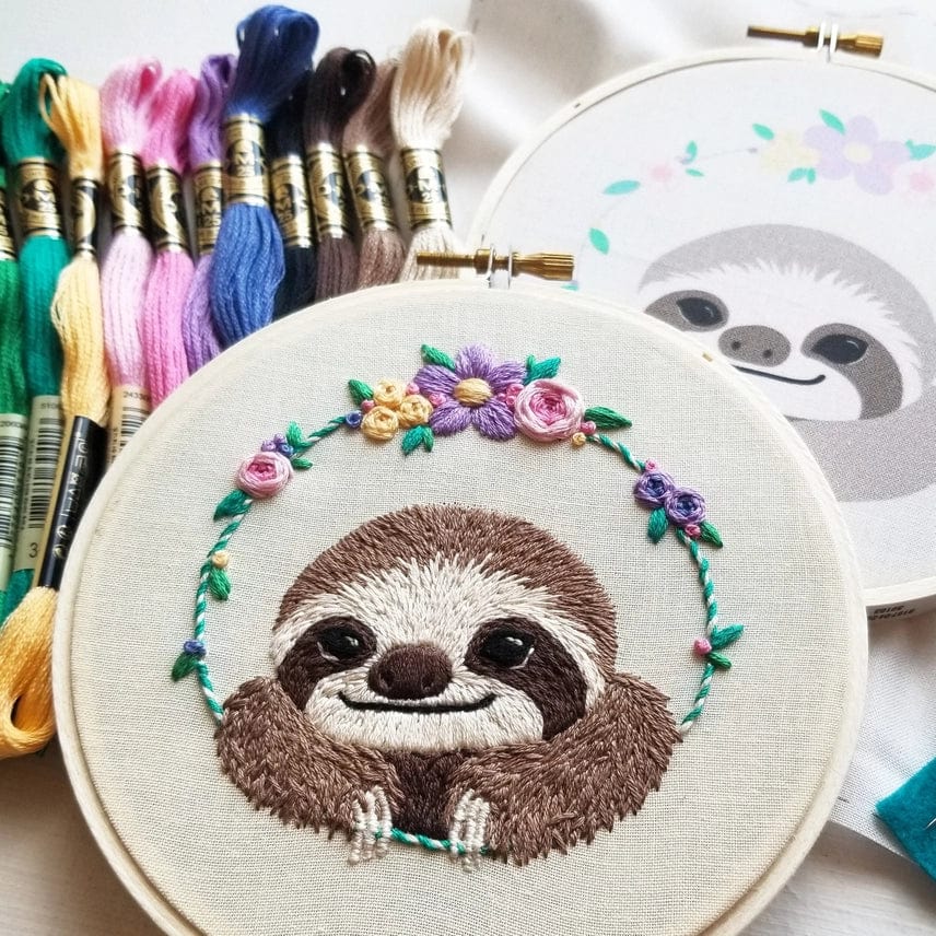 The 5 Beginner Smiling Sloth Embroidery Kit by Jessica Long Embroidery features a stitched sloth face with colorful flowers, embroidery floss in various colors, and a printed pattern—ideal as a DIY gift or for your own creative project.