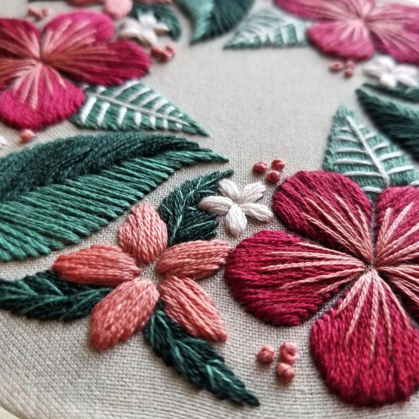 Close-up of colorful floral embroidery—pink, red, and white flowers with green leaves on taupe fabric—from the Jessica Long Embroidery 5 Beginner Taupe Floral Flourish Kit. The threadwork’s details and textures are clearly visible.