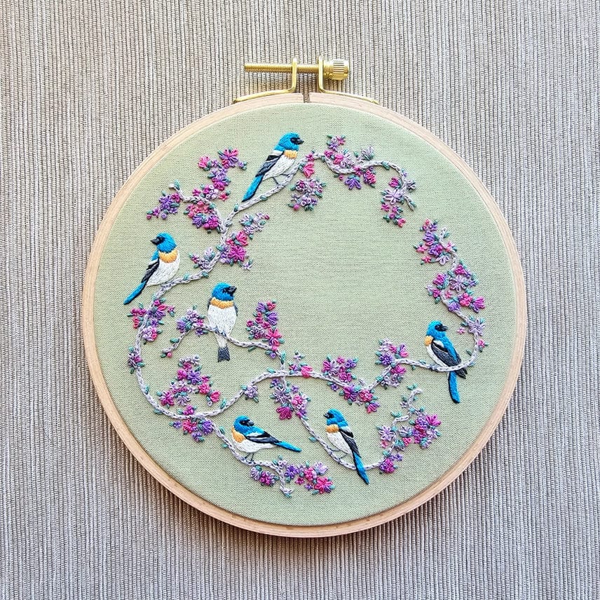 The *Late May Pre-Order* 6 Birds & Blooms Embroidery Kit by Jessica Long Embroidery features vibrant birds on branches with pink and purple flowers, set on a light fabric—ideal for beginners to practice hand embroidery stitches.