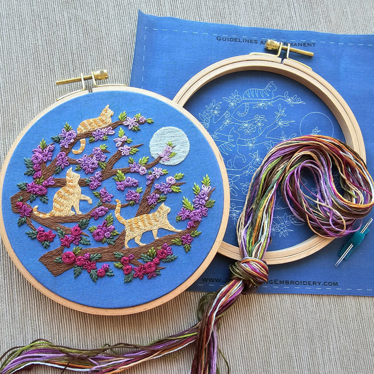 The 6 Beginner Orange Cats & Full Moon Embroidery Kit by Jessica Long Embroidery includes a colorful stitched scene of three orange cats on a tree with purple flowers and a full moon, plus beginner-friendly instructions and multicolored floss.