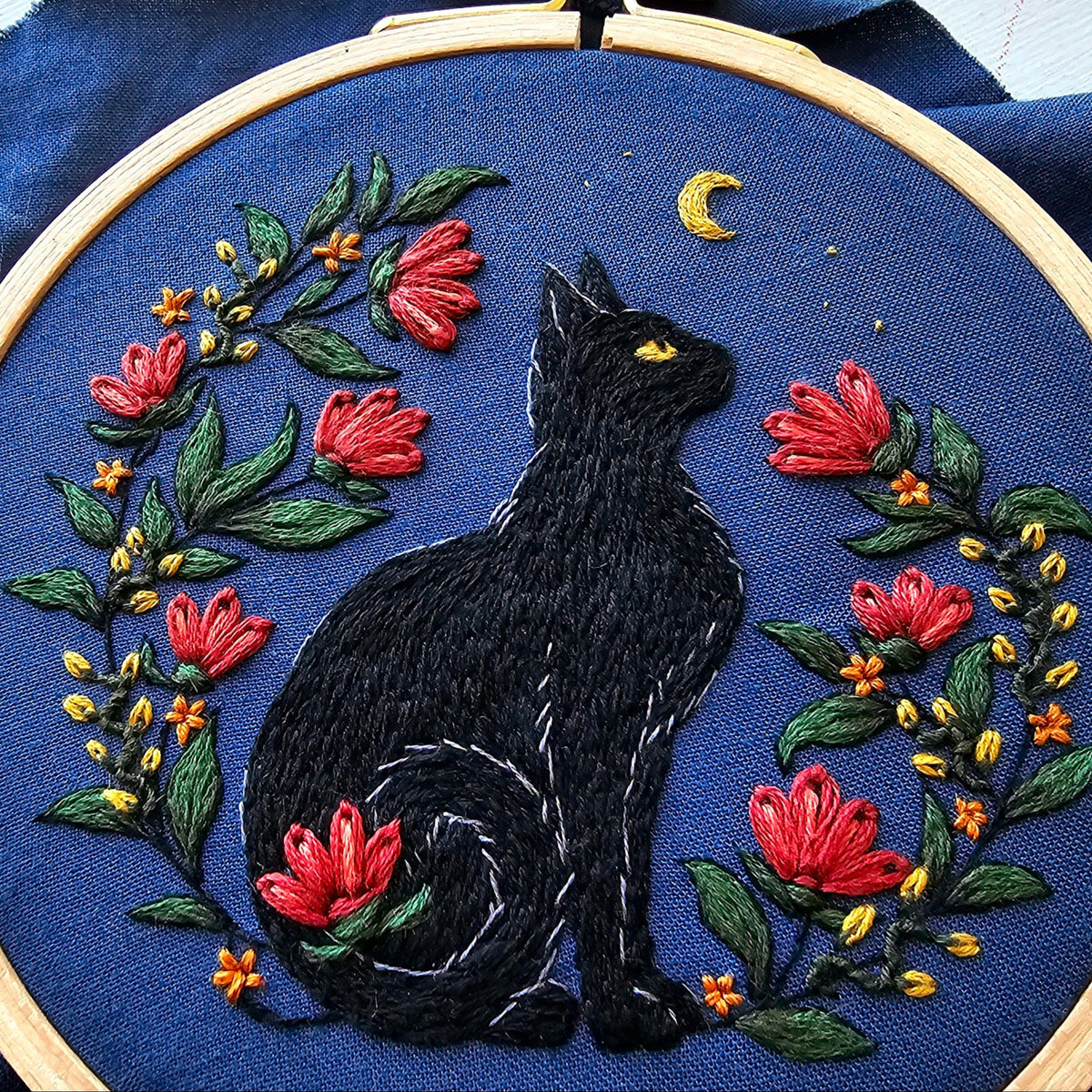 The *Late May Pre-Order* 5 Beginner Stargazer Black Cat Embroidery Kit by Jessica Long Embroidery features a black cat among red and yellow flowers under a crescent moon, all on dark blue fabric in a wooden hoop.