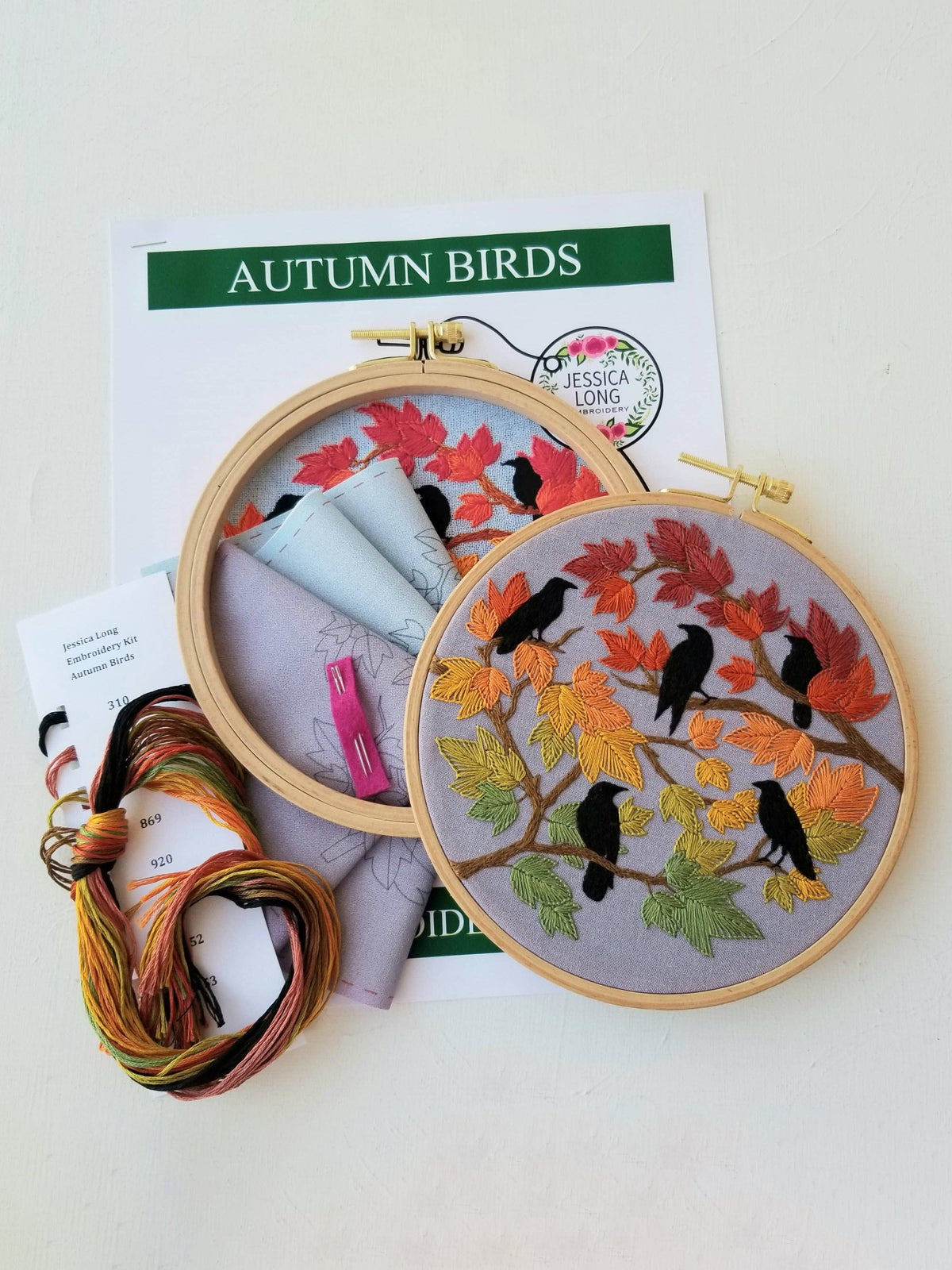 The Jessica Long Embroidery 6 Beginner Autumn Birds Embroidery Kit features a finished hoop with black birds on fall leaves, displayed on the AUTUMN BIRDS pattern and surrounded by floss, needles, and fabric—ideal for beginners.