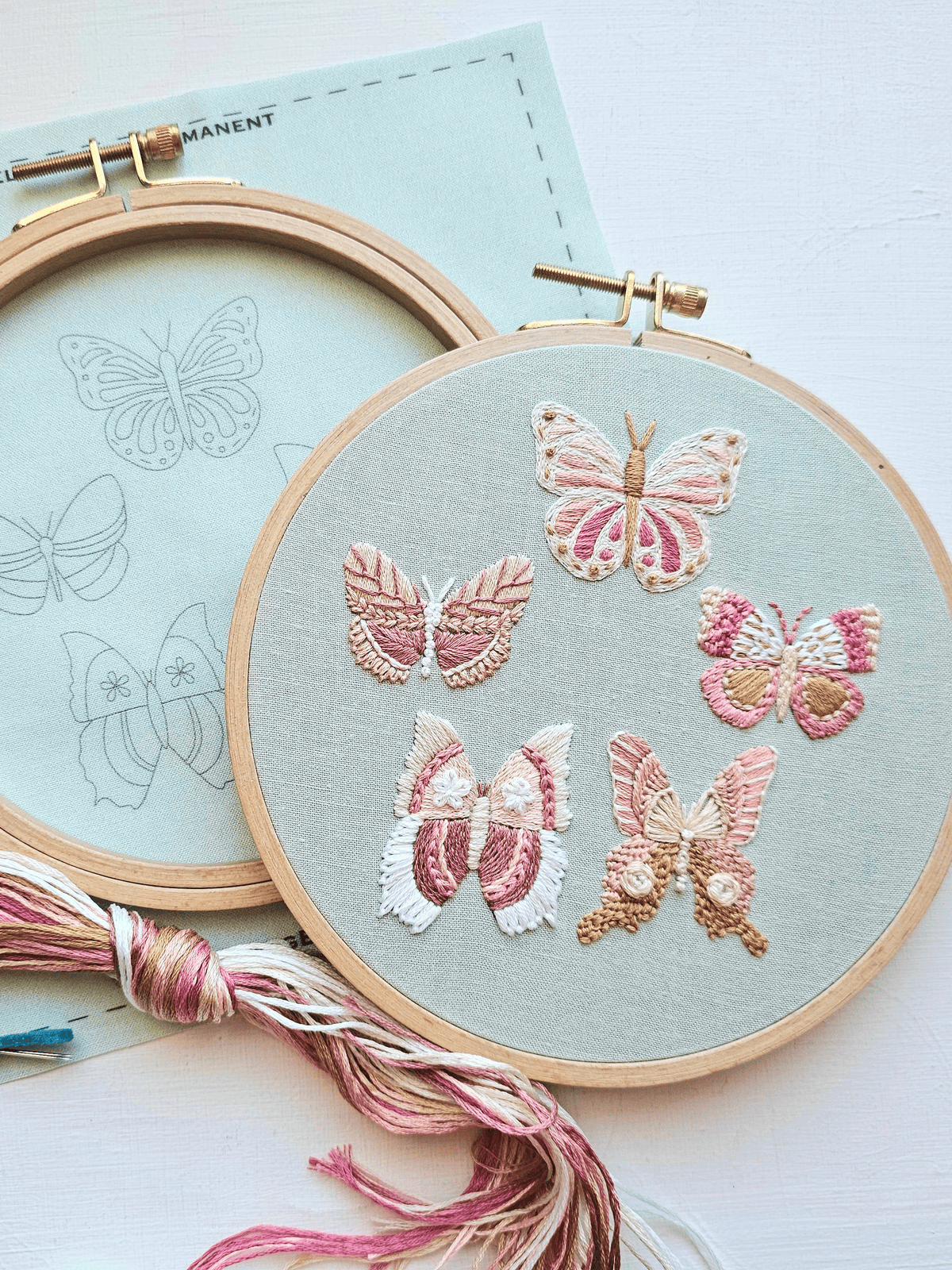The 6 Butterfly Embroidery Kit by Jessica Long Embroidery features a round hoop with six embroidered butterflies in soft pink, cream, and beige. The kit includes a butterfly sampler fabric and matching threads—ideal for beginners.