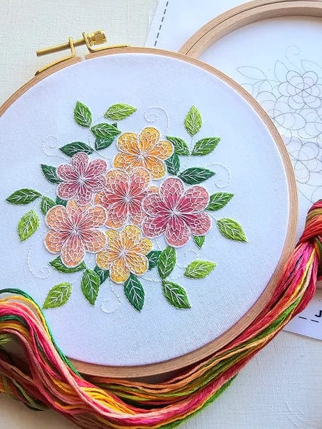 The Jessica Long Embroidery 6 Lacy Flowers Embroidery Kit showcases a finished floral design in pink and yellow with green leaves. Multi-colored threads and a pattern outline are included, ideal for beginners interested in thread painting.