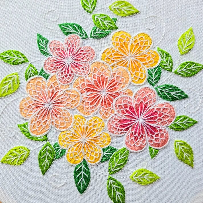 The 6 Lacy Flowers Embroidery Kit by Jessica Long Embroidery features vibrant pink, orange, and yellow flowers with green leaves on white fabric, creating a lively and colorful floral design.