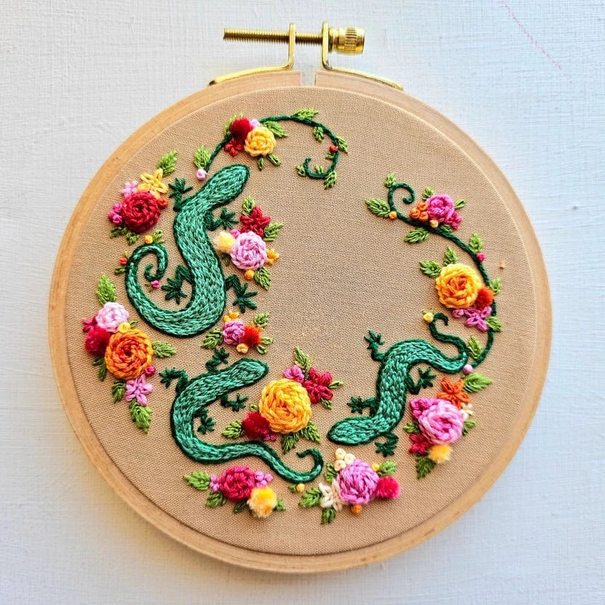 The 6 Beginner Backyard Geckos Embroidery Kit by Jessica Long Embroidery features two green geckos on beige fabric with colorful flowers—ideal for beginners or as inspiration for your next embroidery project.