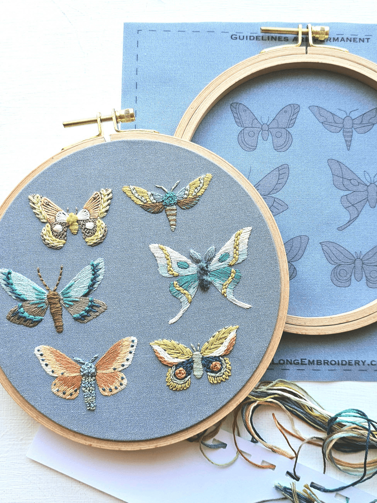 The *Late May Pre-Order* 6 Moth Embroidery Kit by Jessica Long Embroidery features six vibrant moths on blue fabric, with included outlines and floss to inspire your next creative hand embroidery project.