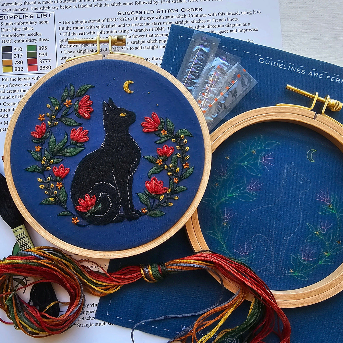 The *Late May Pre-Order* 5 Beginner Stargazer Black Cat Embroidery Kit by Jessica Long Embroidery features a black cat among red flowers under a crescent moon and includes threads, an extra hoop with blue fabric, and instructions.