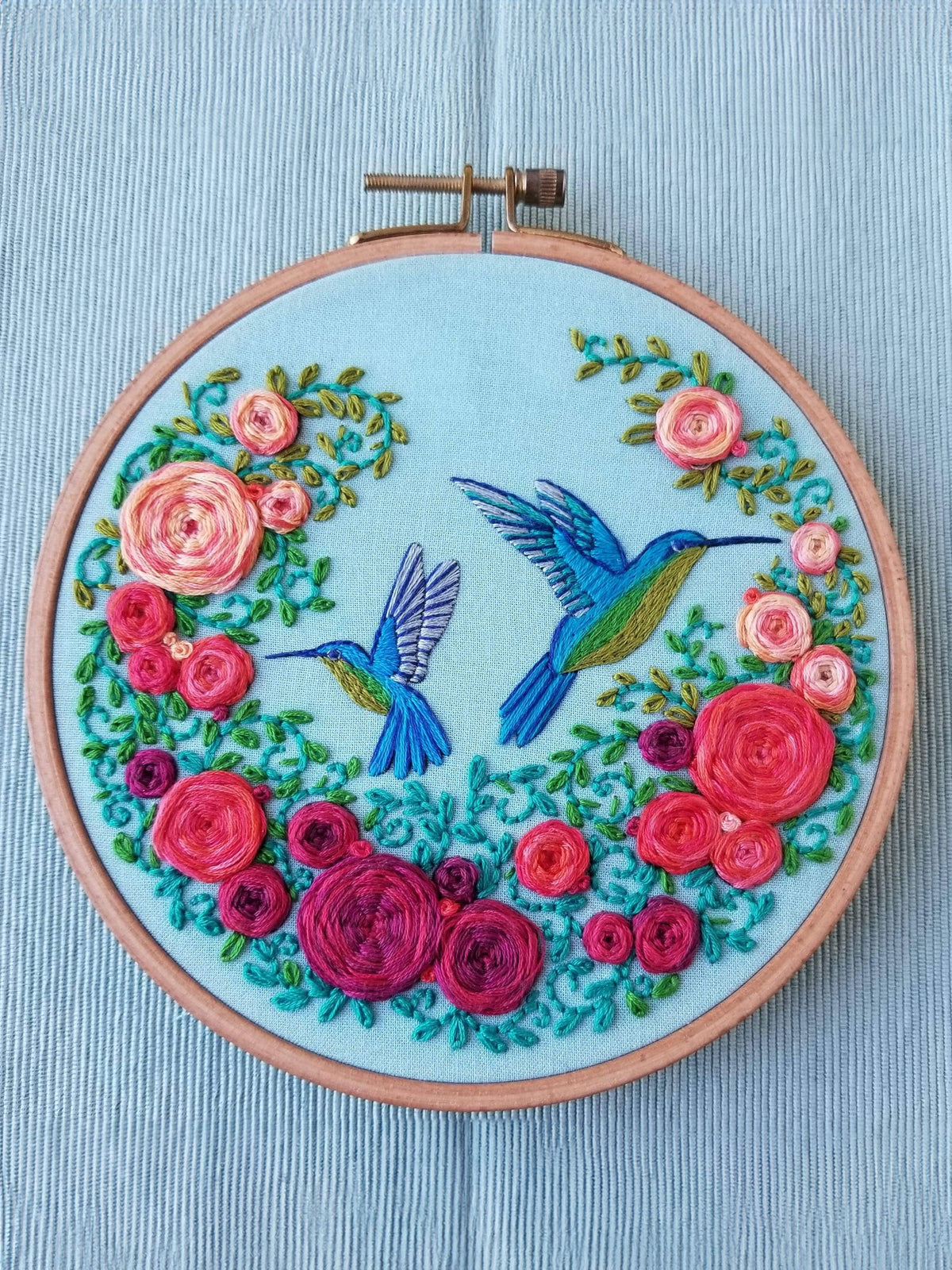 The *Late May Pre-Order* 6 Beginner Summer Hummingbird Embroidery Kit by Jessica Long Embroidery features two blue and green hummingbirds with vibrant flowers stitched on light blue fabric—perfect for any craft collection.
