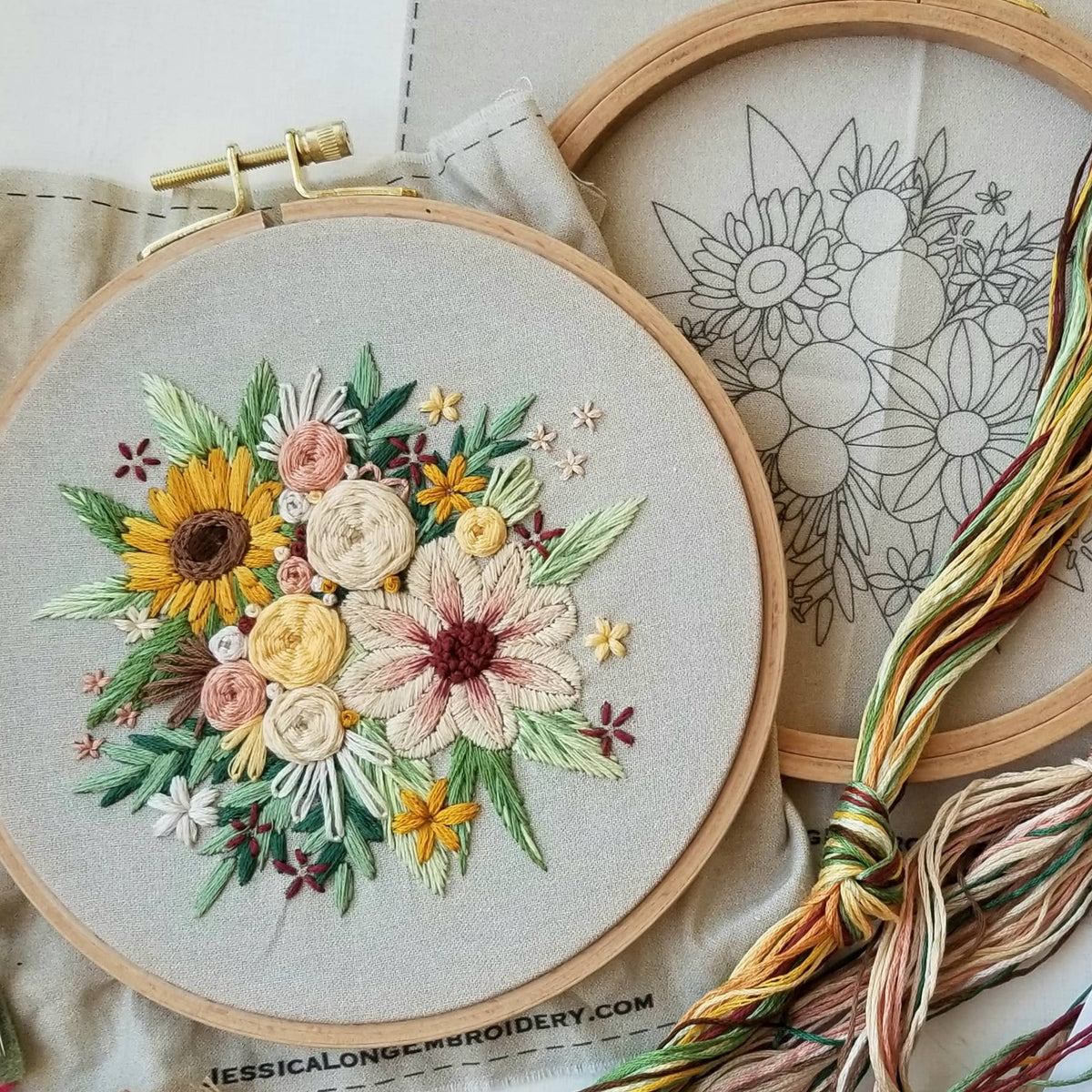 The 6 Beginner Floral Harvest Embroidery Kit by Jessica Long Embroidery features a hoop with colorful stitched flowers, another with a black outlined design, and multicolored threads on a printed bag—perfect for home decor or creative projects.