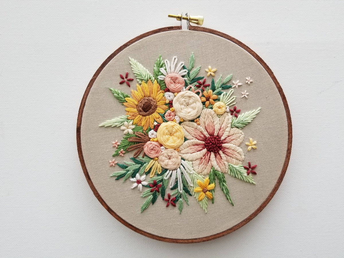 The Jessica Long Embroidery 6 Beginner Floral Harvest Embroidery Kit features a floral design with hand-stitched flowers and leaves in yellow, white, peach, green, and red threads on beige fabric—perfect for home decor.