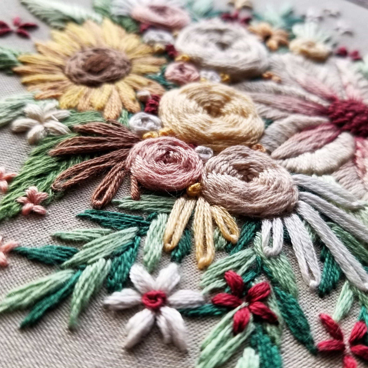Close-up of colorful hand-embroidered sunflowers and roses on fabric from the 6 Beginner Floral Harvest Embroidery Kit by Jessica Long Embroidery. Textured stitches create a unique touch, perfect for vibrant home decor.