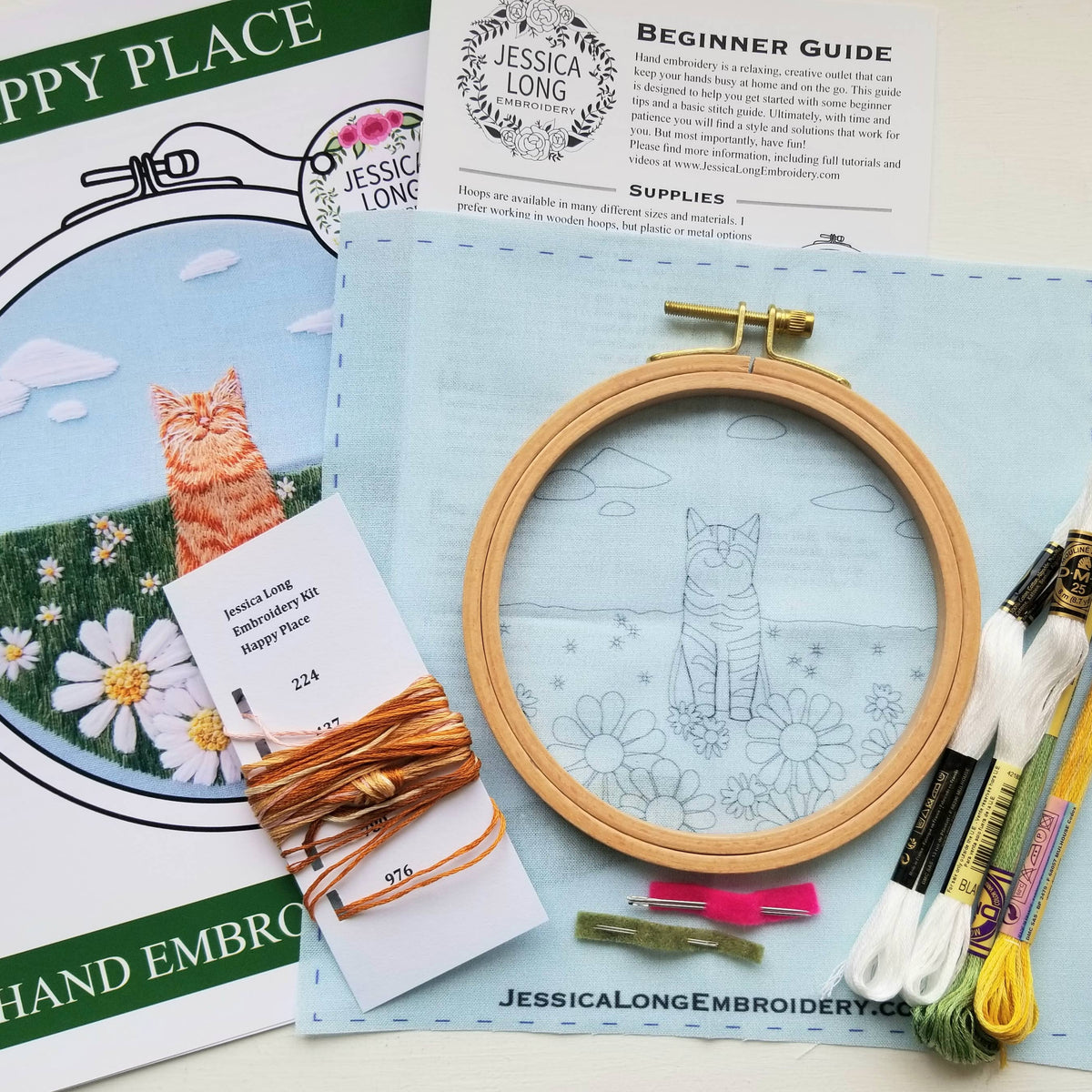 The 5 Happy Cat Embroidery Kit by Jessica Long Embroidery is a perfect beginner hand sewing project, with printed fabric in a hoop, colorful threads, needles, instructions, and a reference image of a cat in garden flowers.