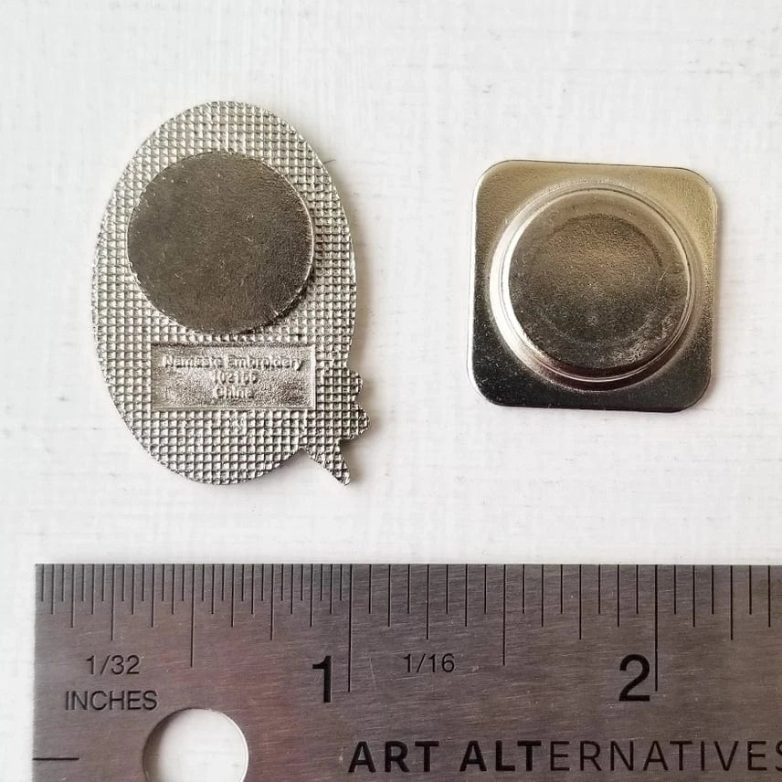 The Chickadee Enamel Needle Minder by Jessica Long Embroidery, featuring an oval design with a round magnet, is shown beside its square magnetic backing and a ruler in inches for scale.