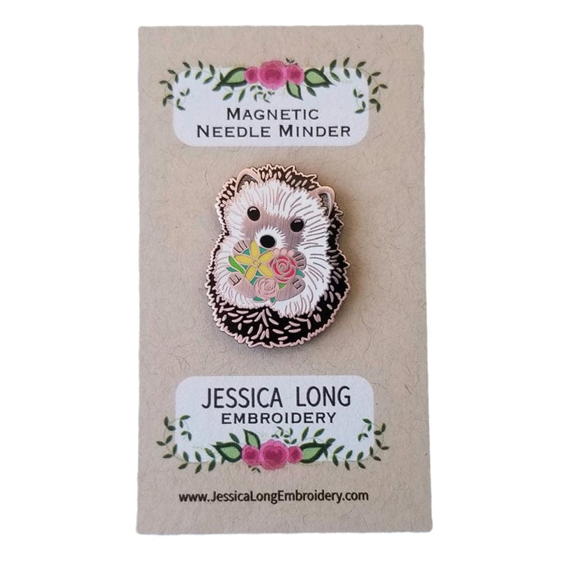 The Hedgehog Enamel Needle Minder by Jessica Long Embroidery keeps your needles secure and adds charm to your stitching. Attached to a decorative floral card, this magnetic pin features a hedgehog holding flowers for a cute touch.