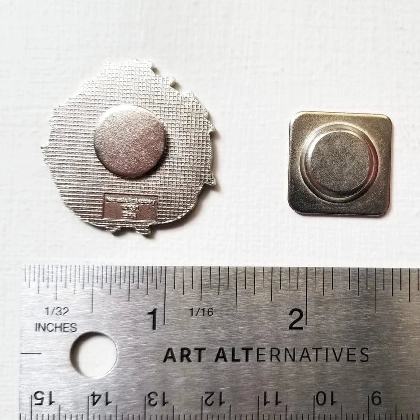 Two small metallic pin backs, shown beside an inch-marked ruler for scale, can be used with the Jessica Long Embroidery Sloth Enamel Needle Minder or other hard enamel pins.