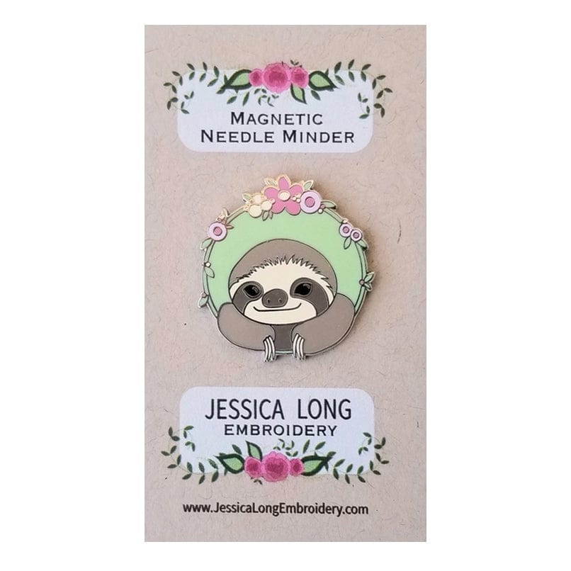 The Sloth Enamel Needle Minder by Jessica Long Embroidery features a hard enamel sloth framed in a floral wreath, shown on a card with pink flowers, Magnetic Needle Minder, and www.JessicaLongEmbroidery.com.