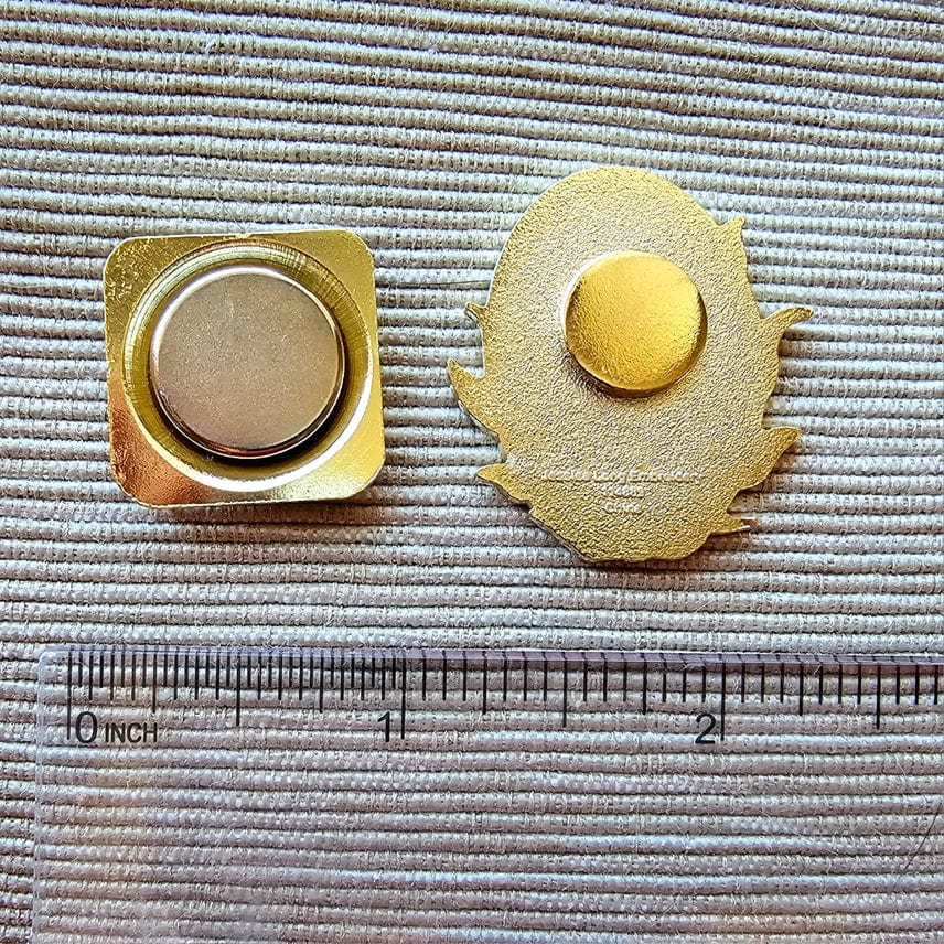The Stargazer Black Cat Enamel Needle Minder by Jessica Long Embroidery, shown on textured fabric with a clear ruler underneath, measures about 1 inch wide and includes both square and leaf-shaped magnetic backs.