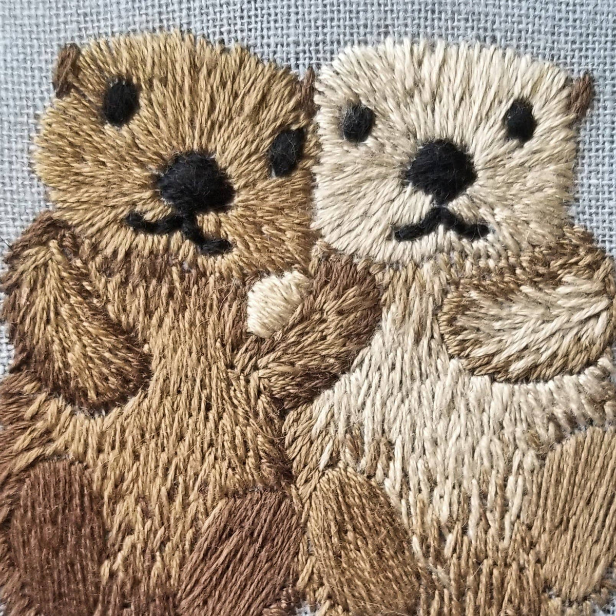The *Late May Pre-Order* 6 Otterly Adorable Embroidery Kit by Jessica Long Embroidery features two otters, brown and beige, cuddling in detailed embroidery—a charming wall art piece and perfect handmade gift.