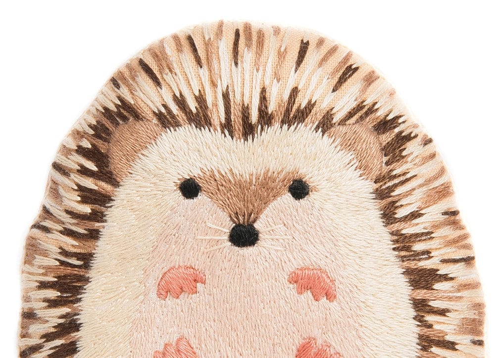 The Hedgehog Embroidery Doll Kit by Kiriki Press features an embroidered patch with a light beige face and belly, brown and cream spines, black eyes, a round nose, and four pink feet—ideal for beginners or doll kits.