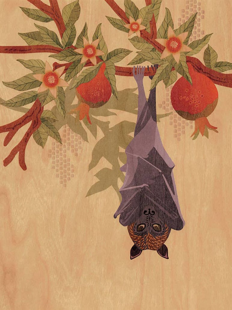 The Fruit Bat and Pomegranate Small Wood Print (11 x 8.5) by Little Gold Fox Designs features a bat among green leaves and red pomegranates on a light wood-textured background, crafted with biodegradable packaging.