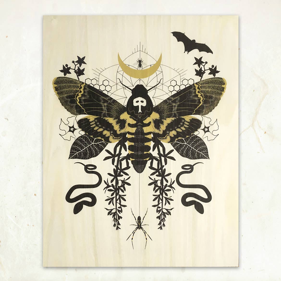 The Hawk Moth Small Wood Print (11 x 8.5) by Little Gold Fox Designs features a death’s-head hawkmoth with a skull pattern, plus leaves, snakes, bats, spiders & a crescent moon—printed on sustainable wood veneer with a light background.