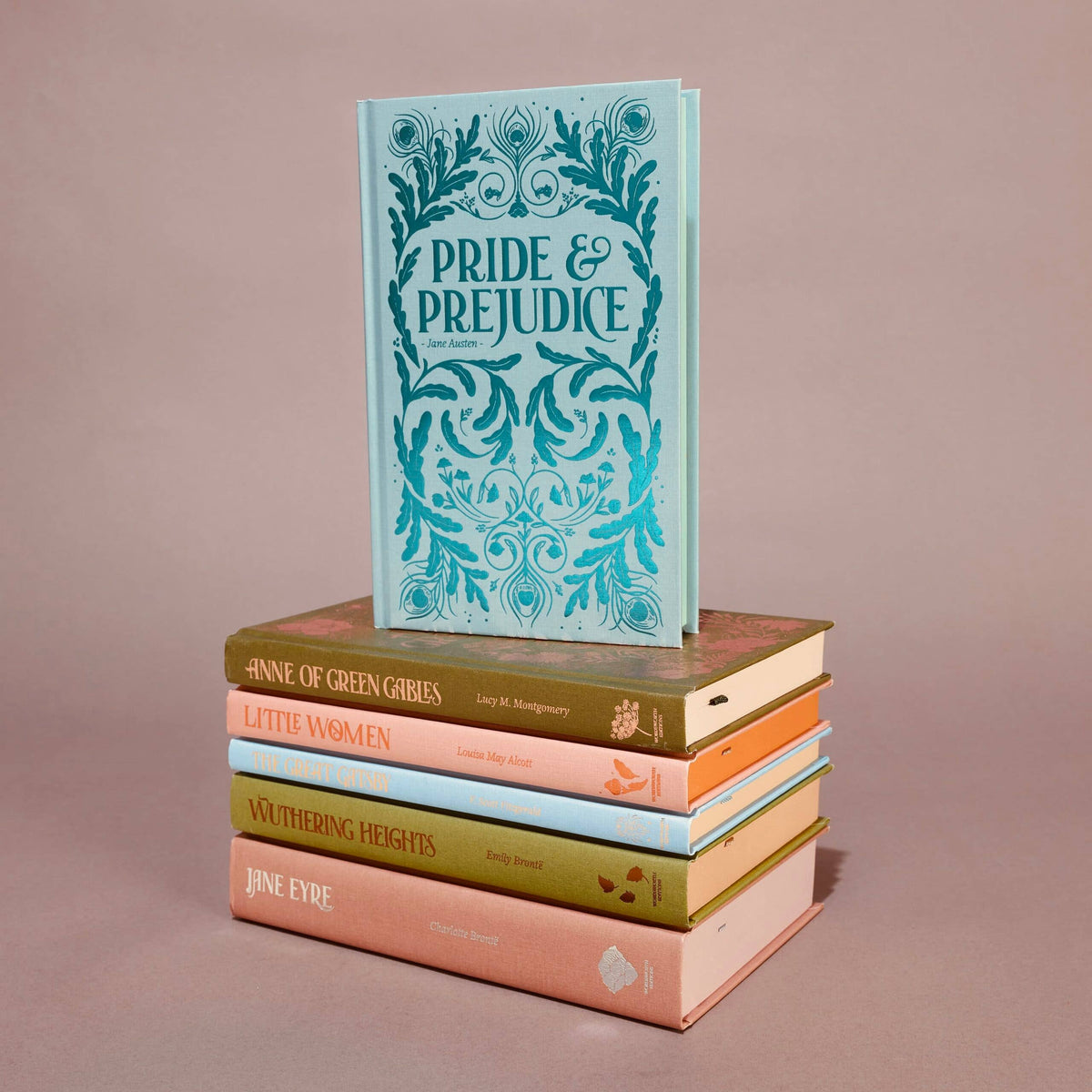 A stack of six classic novels with colorful covers rests on a pink surface. On top stands Jane Eyre by Charlotte Brontë, from Wordsworth Classics, with other English fiction titles arranged horizontally below it.