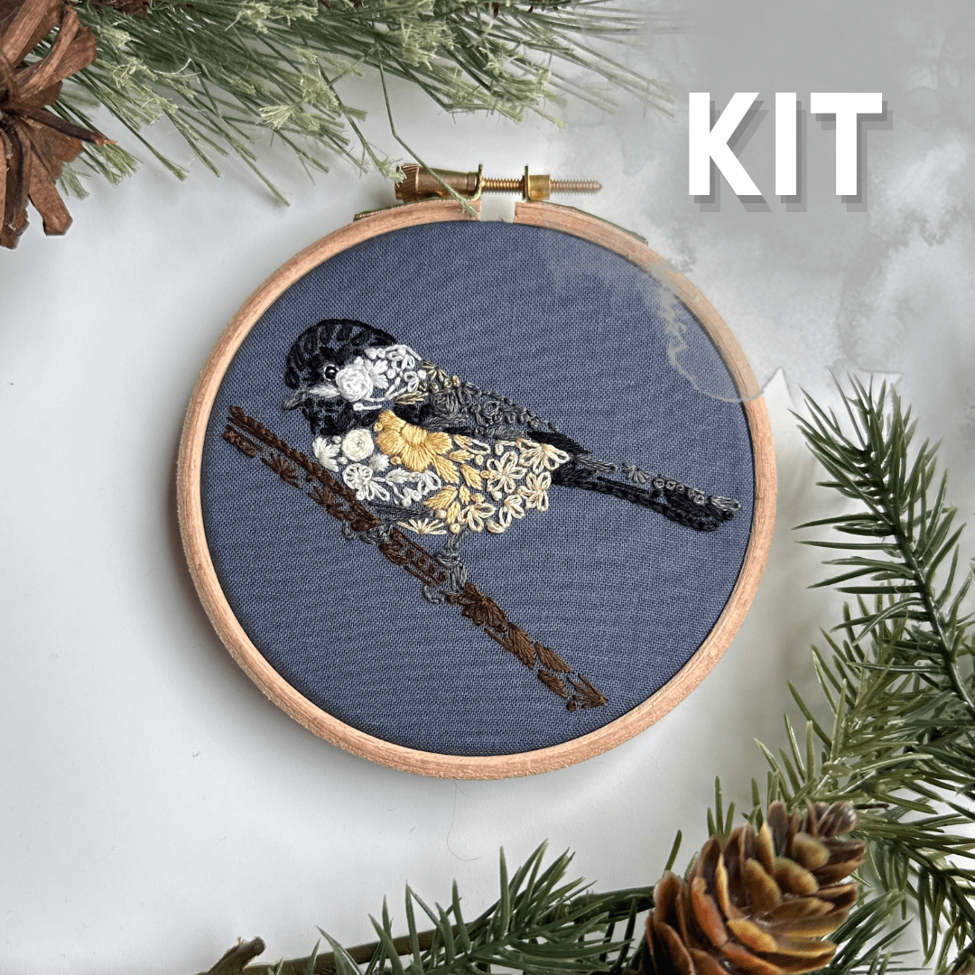 The 4 Beginner Chickadee-dee Embroidery Kit by Nest Embirdery features a black-capped chickadee in a wooden hoop, stitched with yellow, white, and black threads. KIT is marked in bold white letters; perfect for beginners.