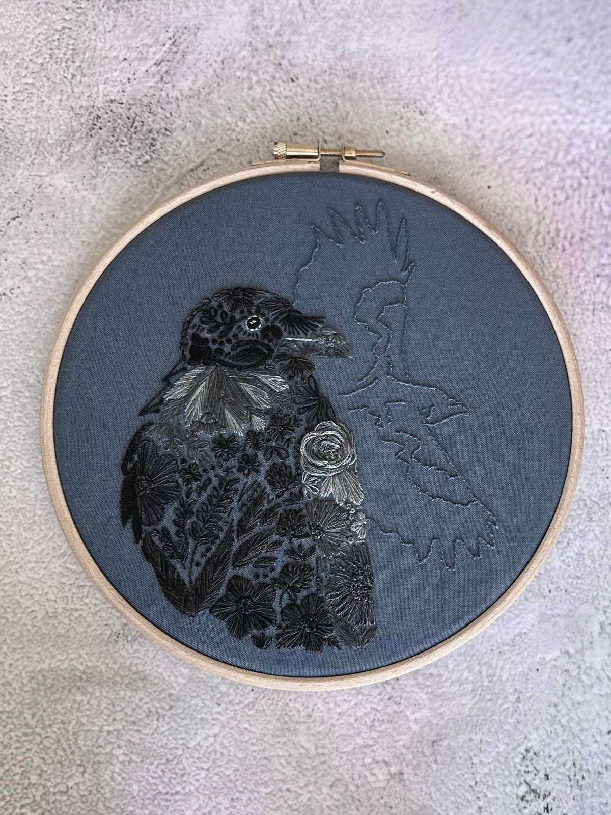 Nest Embirderys 7 Beginner Raven Petals Embroidery Kit features a black floral-stitched raven on dark fabric and a gray bird outline, highlighting a unique stick and stitch style—perfect for beginners.