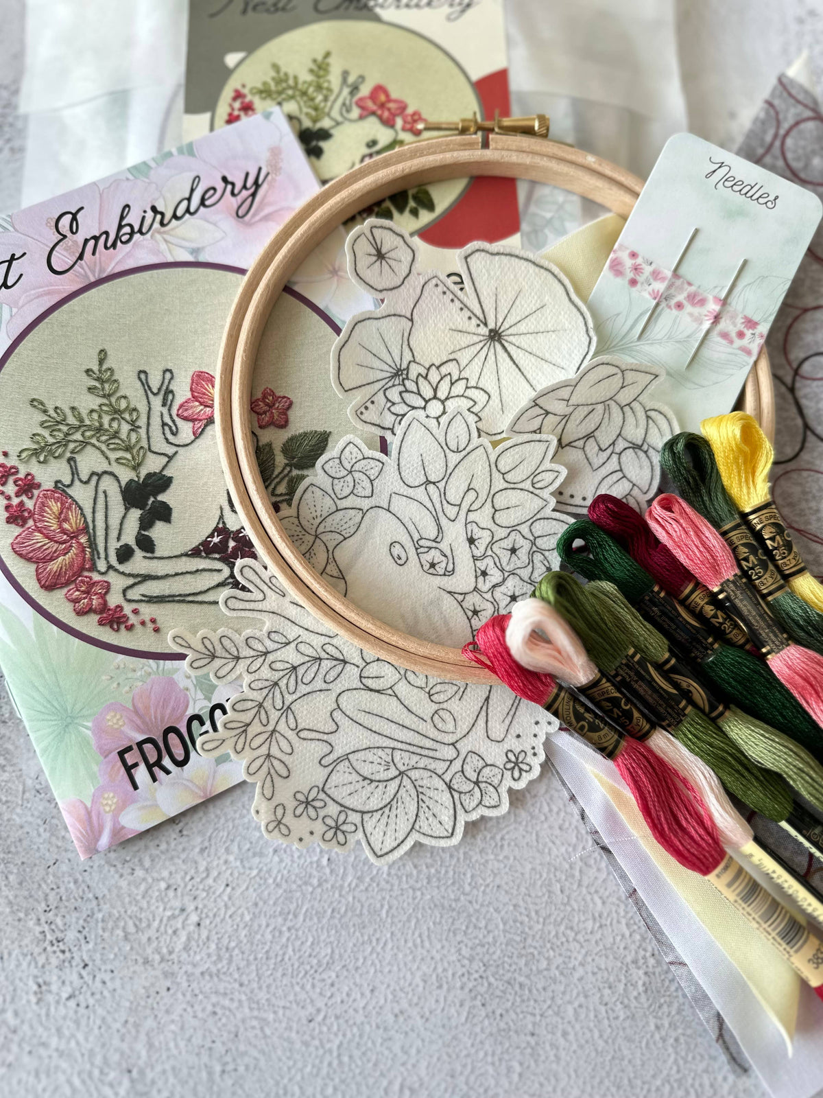 The Nest Embirdery 6 Beginner Froggy Flowers Embroidery Kit includes a wooden hoop, floral frog pattern, colored threads, needles, and instructions—everything an advanced beginner needs to create froggy floral embroidery.