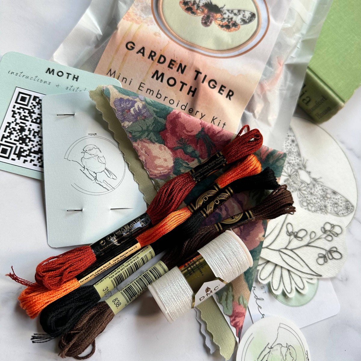 The Nest Embirdery 4 Beginner Garden Tiger Moth Embroidery Kit includes colored floss, needle, fabric, thread, printed patterns, and an instruction card with a QR code—ideal for insect embroidery fans.